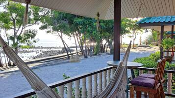 A wooden deck with a hammock, a table with chairs, and a view of the beach and ocean.