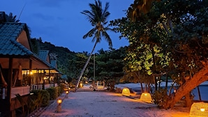 A beachside resort with a wooden building, palm trees, and beach huts. - Sense Asia Beach Resort (Ko Pha-ngan)