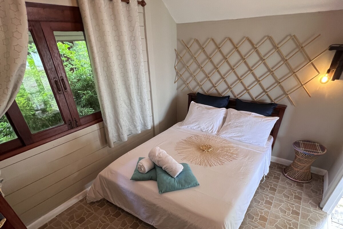 A bedroom with a bed, a window with curtains, a headboard with a geometric pattern, and a woven basket.