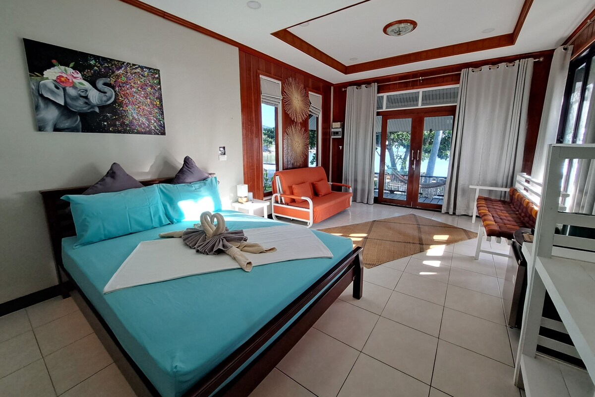 A hotel room with a bed, a sofa, a dining table, and a large window with curtains.