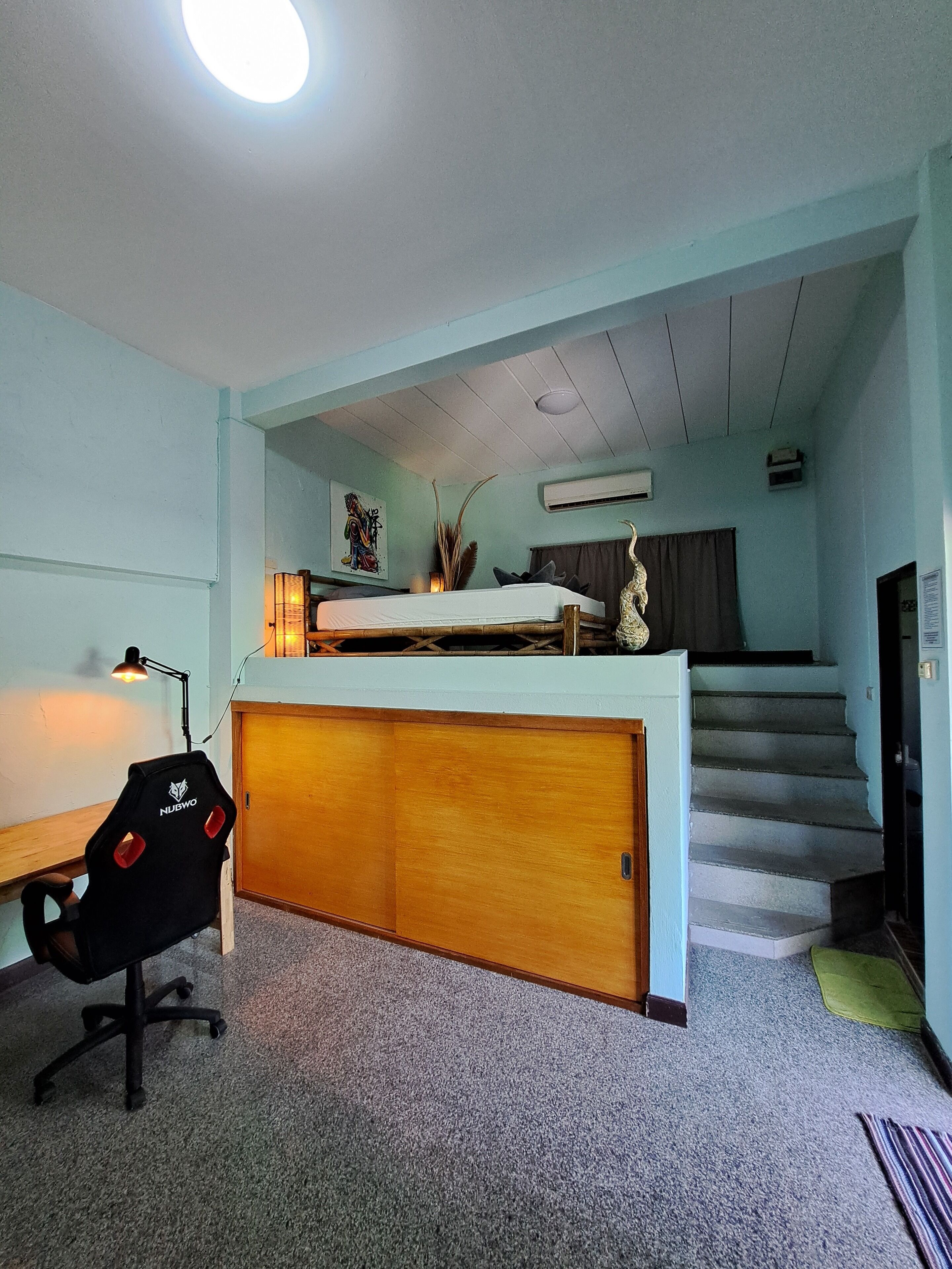 Una habitación compacta con literas, un escritorio con silla, una lámpara y una escalera que sube a un nivel superior.