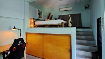Una habitación compacta con literas, un escritorio con silla, una lámpara y una escalera que sube a un nivel superior.