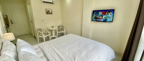 A hotel room with a bed, a small table with two chairs, an air conditioning unit, and a painting on the wall.