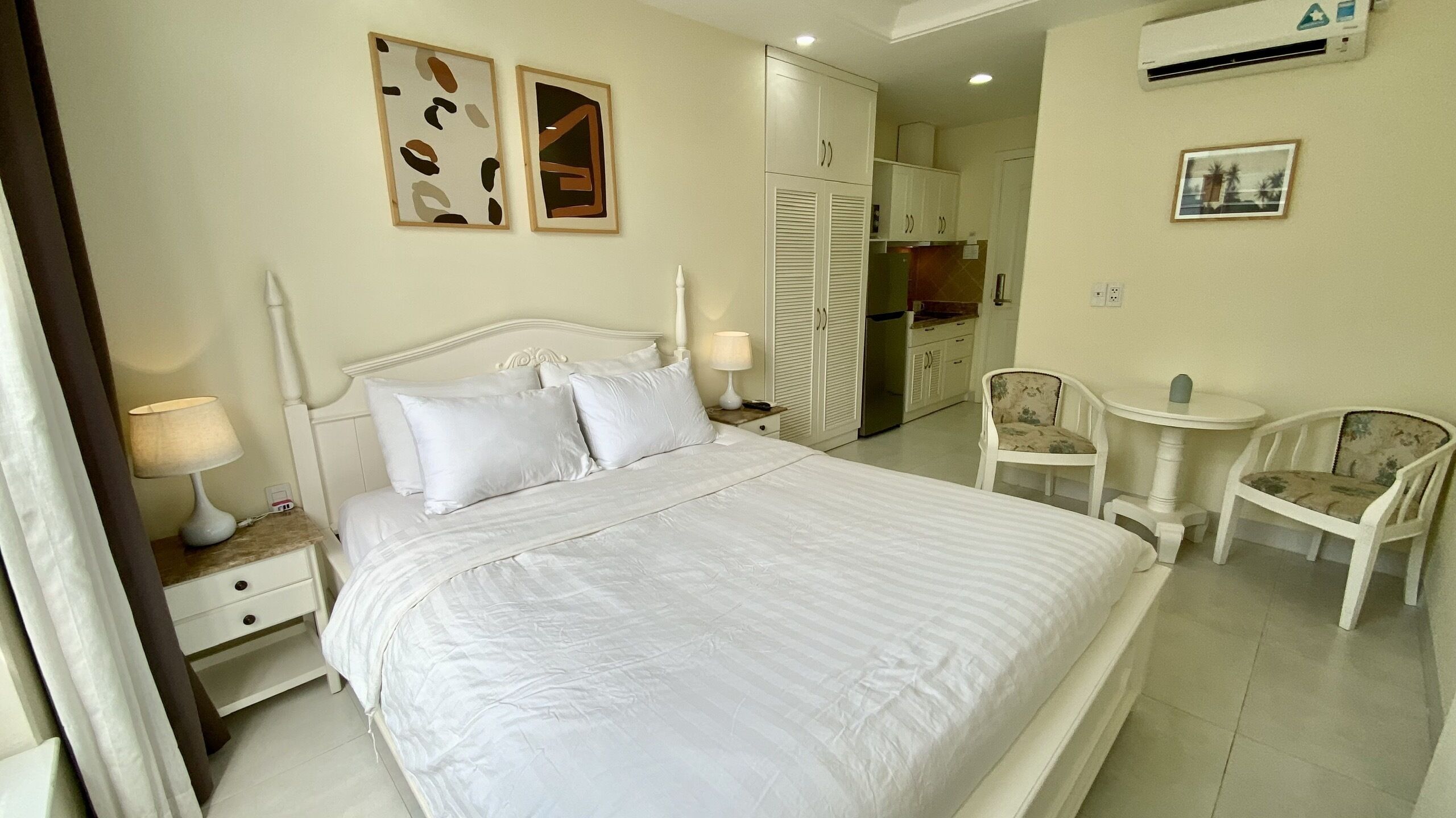 A neatly arranged bedroom with a large bed, bedside lamps, a chair, and a small table.