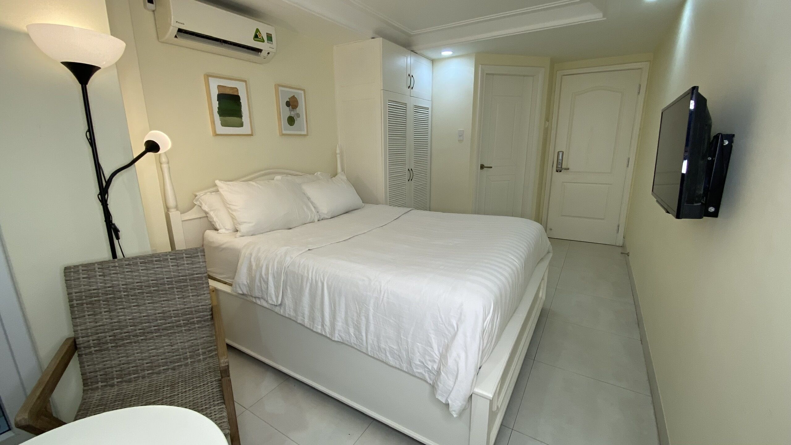 A bedroom with a bed, a bedside table, a lamp, an air conditioner, and a TV mounted on the wall.