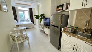 A compact hotel room with a kitchenette, a bed with a balcony, and a dining area.
