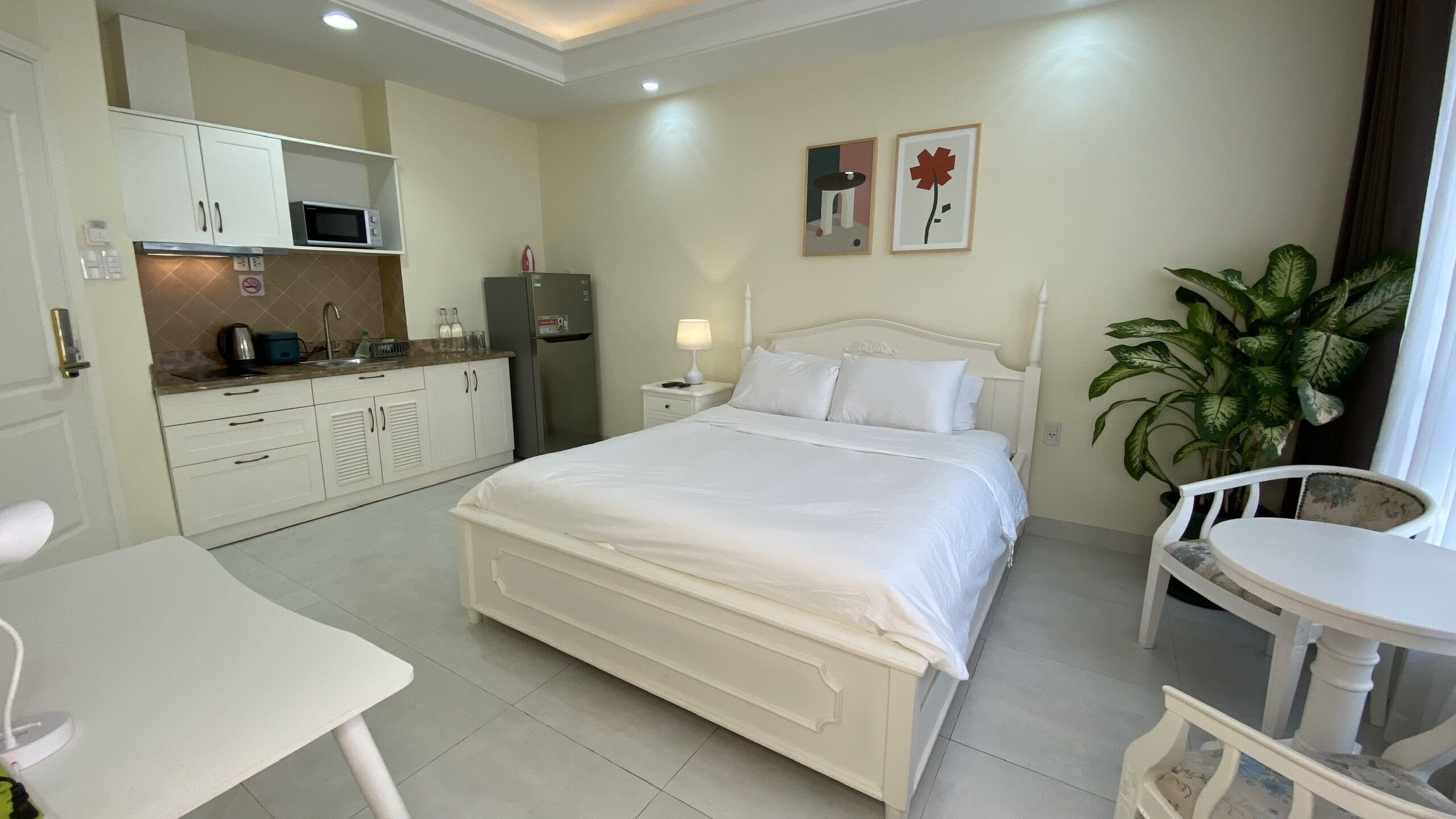 Habitación de hotel con cama, una mesita, una silla, kitchenette y una planta en maceta.