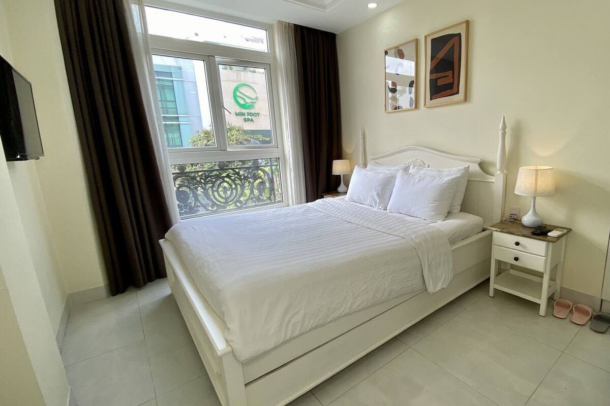 Une chambre d’hôtel avec un lit, des tables de chevet, une lampe, une chaise et une vue sur l’extérieur.