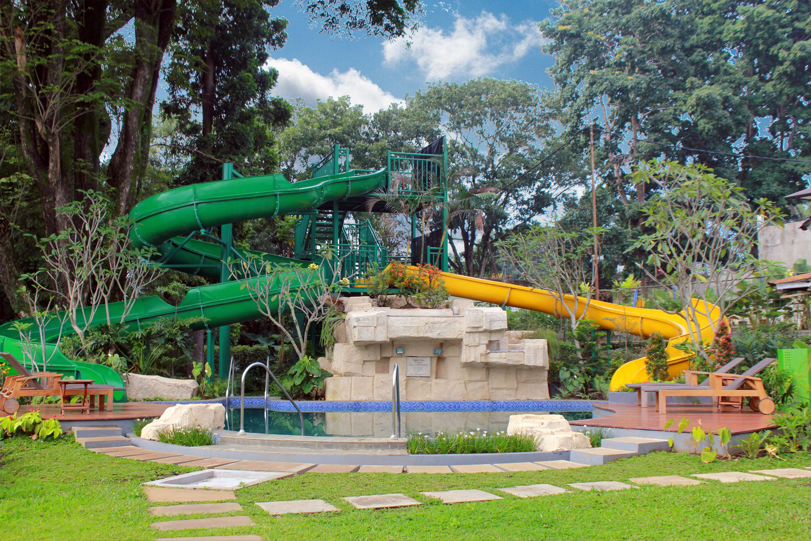 A water park with two slides, a pool, and surrounding greenery.