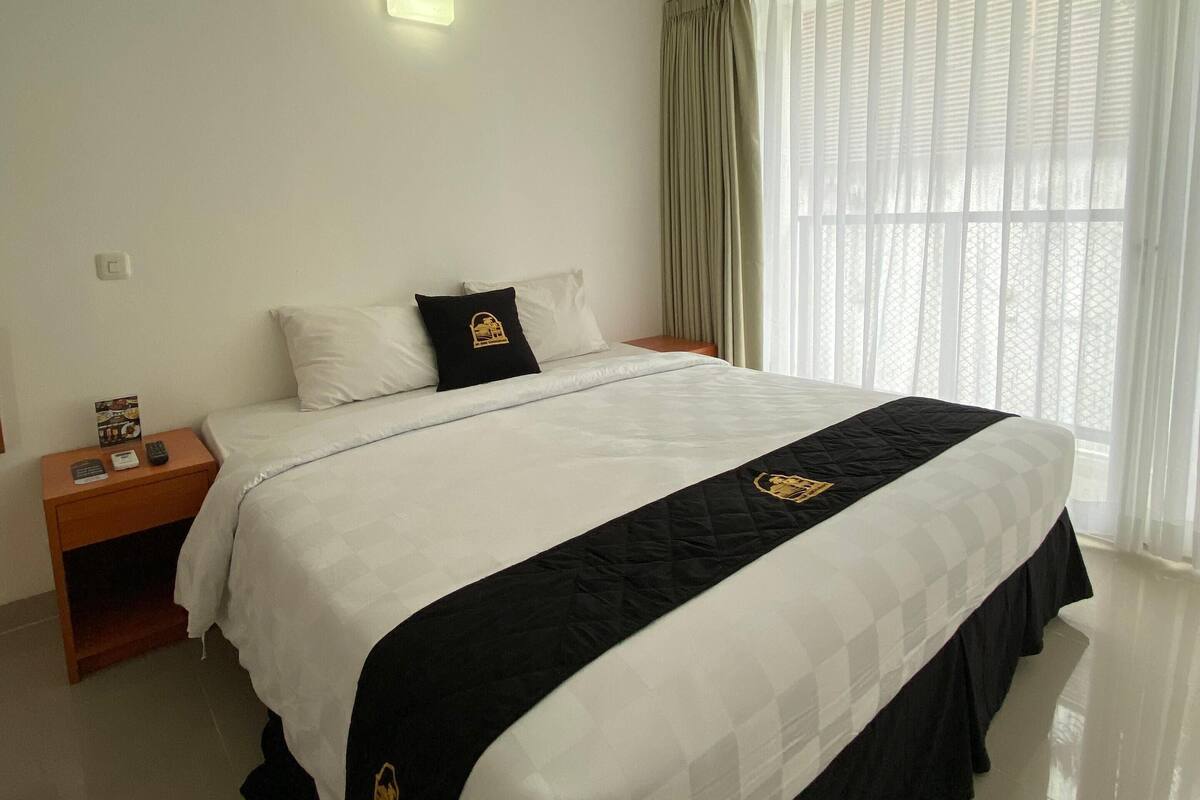 A hotel room with a large bed, a nightstand, a bedside table, and a window with curtains.