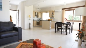 Ein modernes Wohnzimmer mit Sofa, einem Essbereich mit Tisch und Stühlen sowie einer Küche mit Schränken und Geräten.