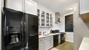Una cocina moderna con un refrigerador negro, armarios blancos, una cafetera y una estufa.
