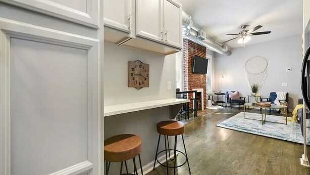 Una cocina moderna con armarios blancos, una pared de ladrillo decorativa y un comedor con mesa redonda y taburetes de bar.