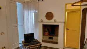 A room with a fireplace, a laptop on a small table, and a door with a yellow handle. - Appartamento al mare ad Ugento nel Salento (Ugento)