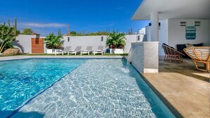 Piscina cristalina con sillones de descanso y un edificio blanco con un letrero que dice 'SAND BEACH PARADISE'.