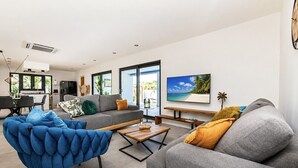 Una sala moderna con un sofá gris, un sillón azul y un televisor mostrando una escena de playa.