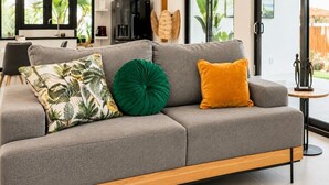 Una sala moderna con un sofá seccional gris, una pequeña mesa redonda de madera y una escultura decorativa de una mariposa.