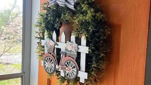 Een houten deur met een decoratieve krans en een oude fiets.