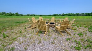 Een cirkel van houten Adirondack-stoelen rond een vuurkuil in een open veld.