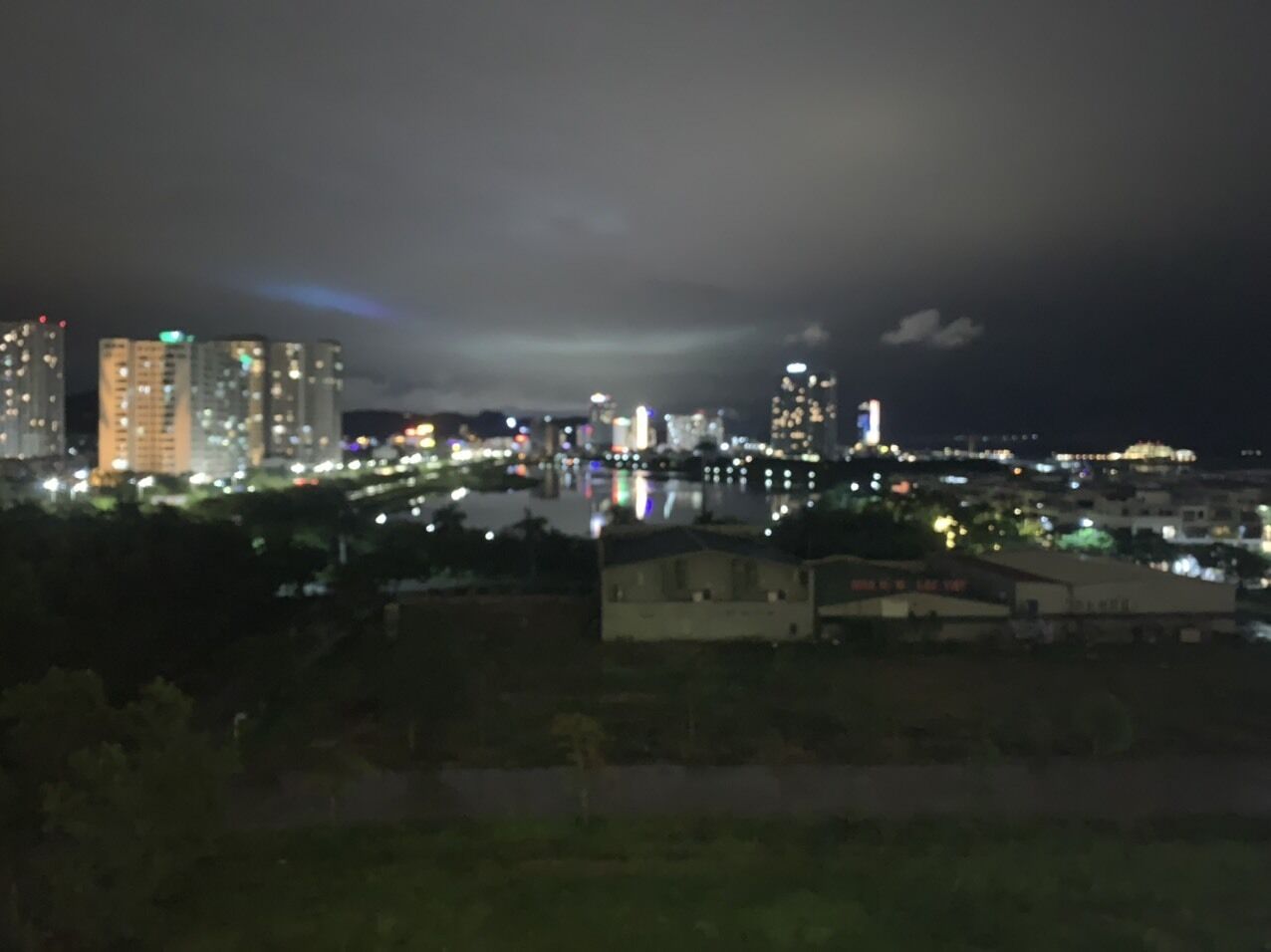 Un paisaje urbano nocturno con edificios iluminados y un cuerpo de agua que refleja luces.
