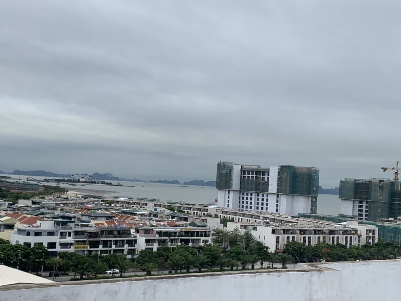 Un paysage urbain côtier, avec un mélange de bâtiments résidentiels et commerciaux, dont un imposant immeuble à plusieurs étages en construction.