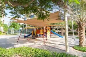 Explore the playground area with slides and climbing elements amidst lush palm trees and a shaded canopy.