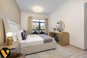 A bedroom with a bed, bedside table, lamp, dresser, and a window with curtains.
