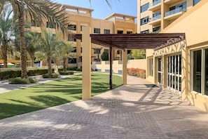 A courtyard with a pergola, palm trees, and a building with large windows. - Vogue | The Greens near Emirates Mall | Ski Dubai (Dubai)