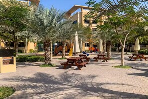 A courtyard with picnic tables, palm trees, and a building in the background. - Vogue | The Greens near Emirates Mall | Ski Dubai (Dubai)
