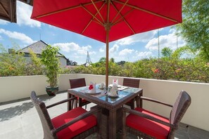 A balcony with a table and chairs, a red umbrella, and potted plants.