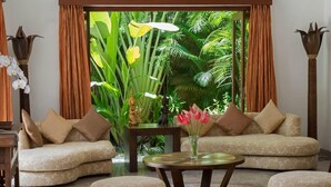 A living room with a sofa set, a coffee table, and a view of tropical foliage through large windows. - Villa Kalimaya (Seminyak)