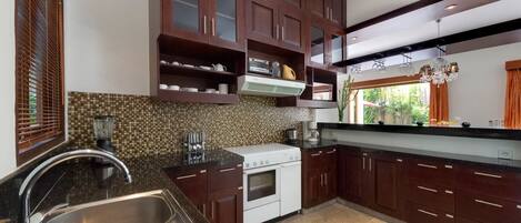 A modern kitchen with dark wooden cabinets, a tiled backsplash, stainless steel appliances, and a large window with curtains.