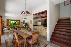 A spacious living room with a dining area, a kitchen, and a staircase. - Villa Kalimaya (Seminyak)