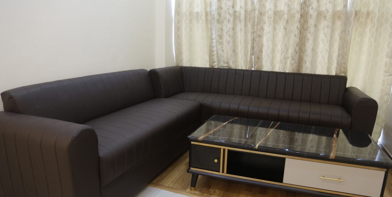 A dark-colored sofa with a glass-top coffee table and a small drawer unit.
