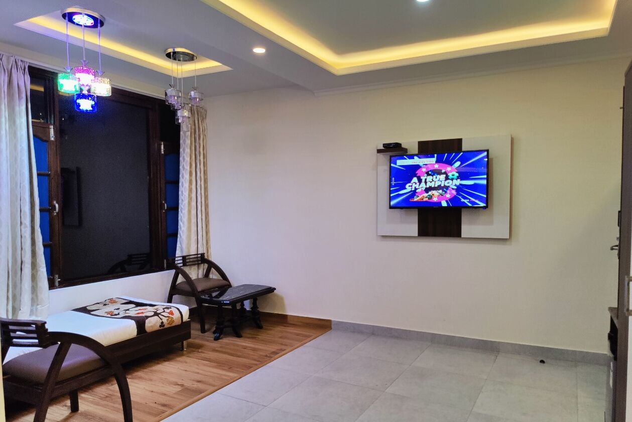 Ein Wohnzimmer mit Flachbildfernseher an der Wand, einer Couch, einem Couchtisch und einem kleinen Tisch mit Stühlen.