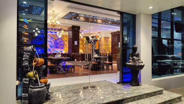 En modern restaurang med en entré av glas, en kristallkrona och en Buddha-staty.