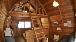 Una cabaña de madera con habitación en el altillo, una escalera, una kitchenette pequeña y una ventana.