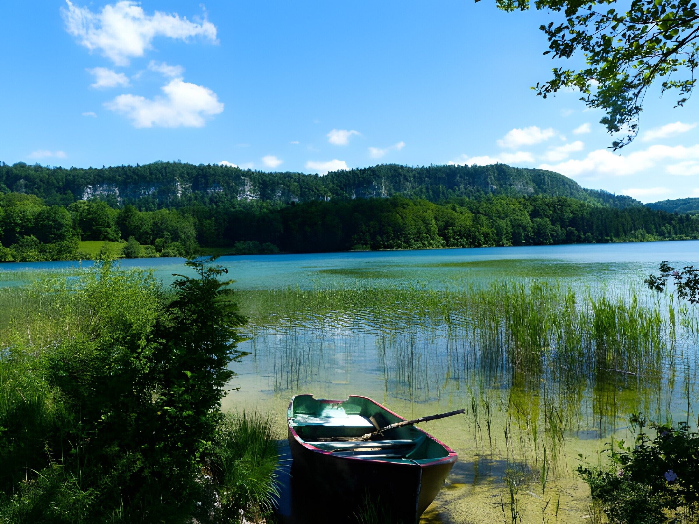 Un llac tranquil amb una barca amarrada a la riba, envoltat de verdura exuberant i turons al fons.