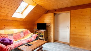Une pièce chaleureuse avec un plafond en pente, un canapé, une petite table, un meuble et un téléviseur.