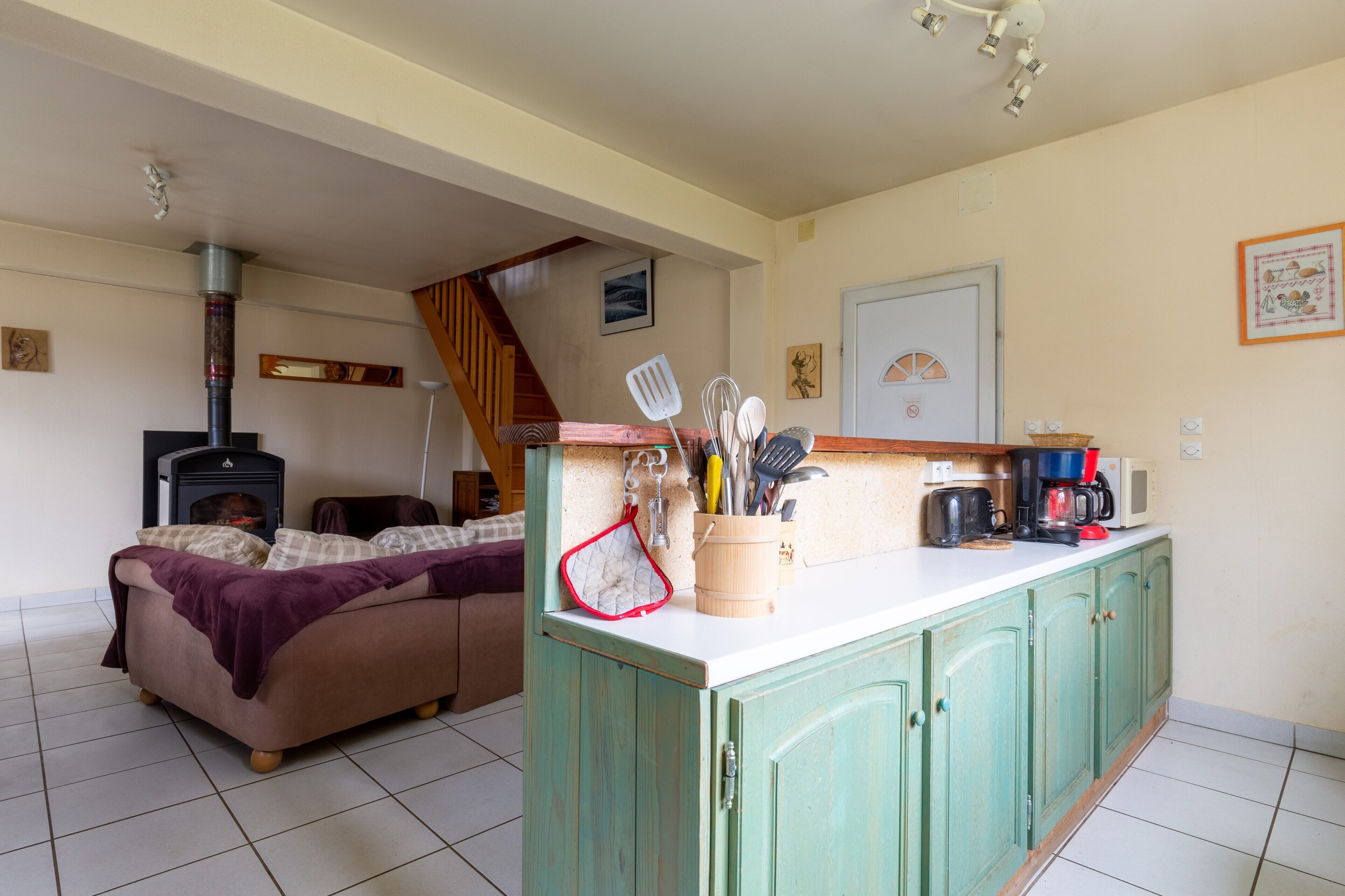 Ein gemütlicher Wohnbereich mit einer Couch, einem Kamin, einer Küche mit Arbeitsplatte und Schränken sowie einer Treppe, die zu einer weiteren Ebene führt.
