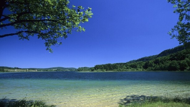 Un lac aux eaux limpides, entouré de verdure et de collines.