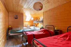 A cabin with wooden walls, a bunk bed, a single bed, a desk, and a chair.