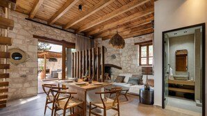 Un interior rústic amb una paret de pedra, sostre de fusta i zona de menjador amb taula i cadires.