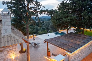 Area piscina con pareti in pietra, una pergola in legno e mobili da esterno.