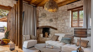 Una habitació rústica amb parets de pedra, una llar de pedra, un sostre de fusta, un sofà blanc i una taula de centre rodona.