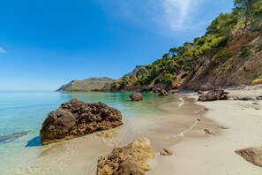 A beach with clear water, rocks, and a mountainous backdrop.