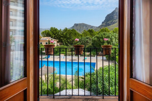 A balcony with a view of a swimming pool, potted plants, and a mountainous landscape.
