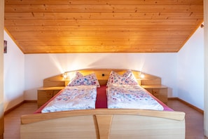 Una camera da letto con soffitto in legno, un letto con lenzuola a motivi floreali e un comodino con una lampada.