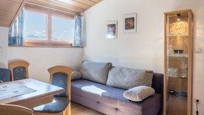 Una habitación acogedora con sofá, una mesa de comedor, sillas, una ventana con cortinas y una vitrina con adornos.
