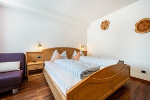 Un lit en bois avec une tête de lit, deux tables de chevet, un canapé violet et deux appliques murales.